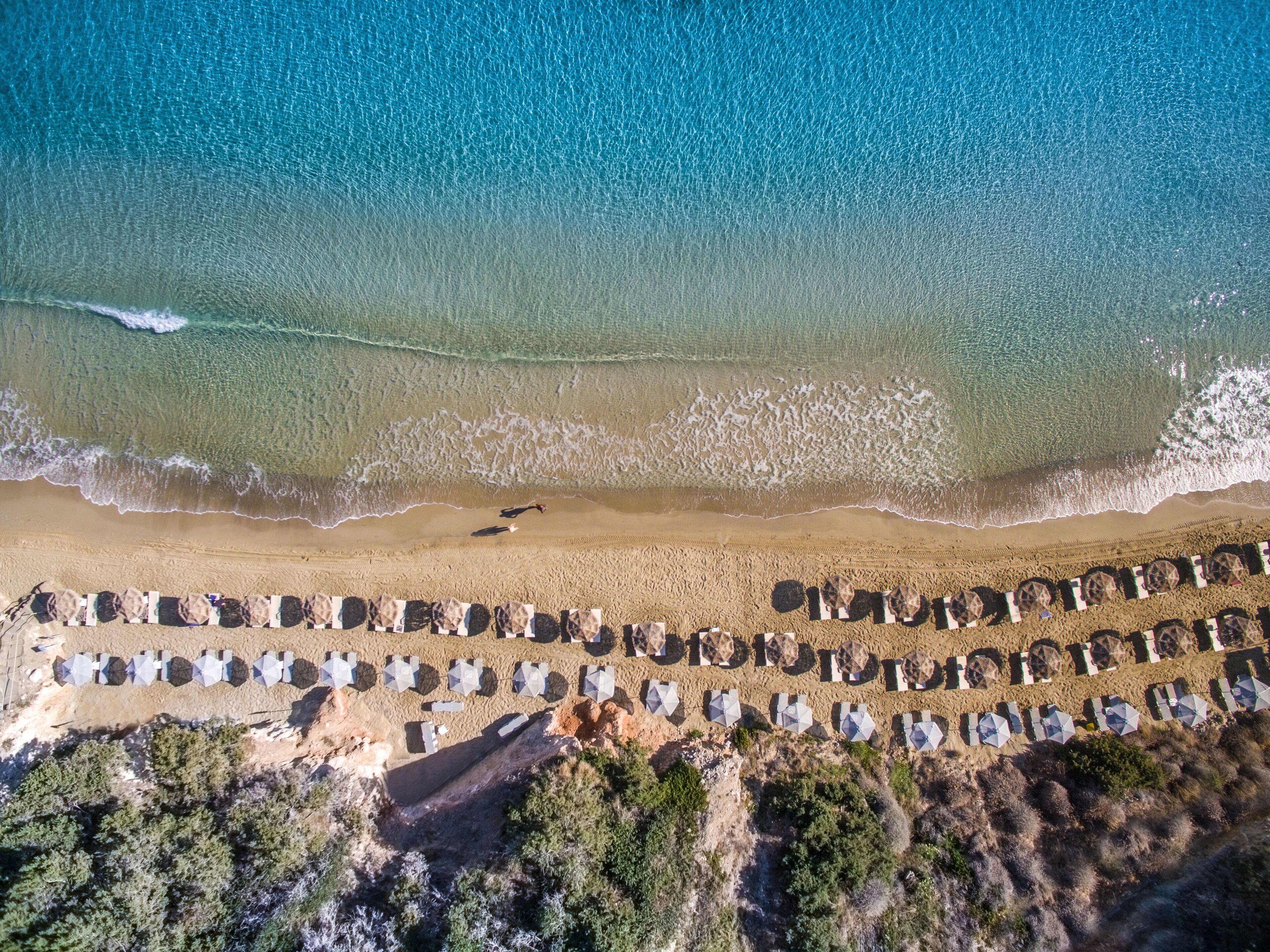 An aerial view of a beach with rows of umbrellas and a person walking along the shore.