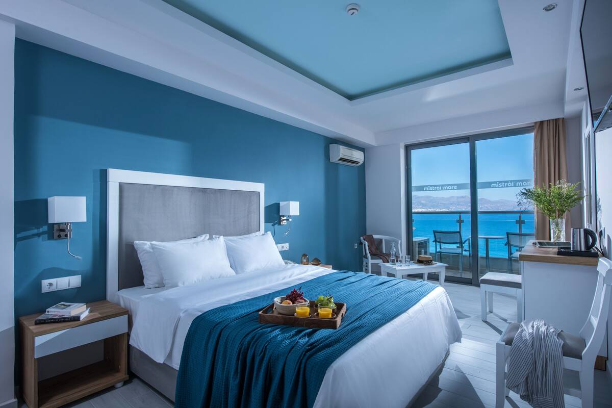 Ein modernes Hotelzimmer mit einem großen Bett, einem Frühstücksbrett, einem Schreibtisch und Meerblick.