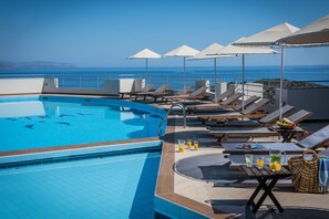 A rooftop pool area with lounge chairs and umbrellas, overlooking a clear blue sea. - Mistral Mare (Agios Nikolaos)