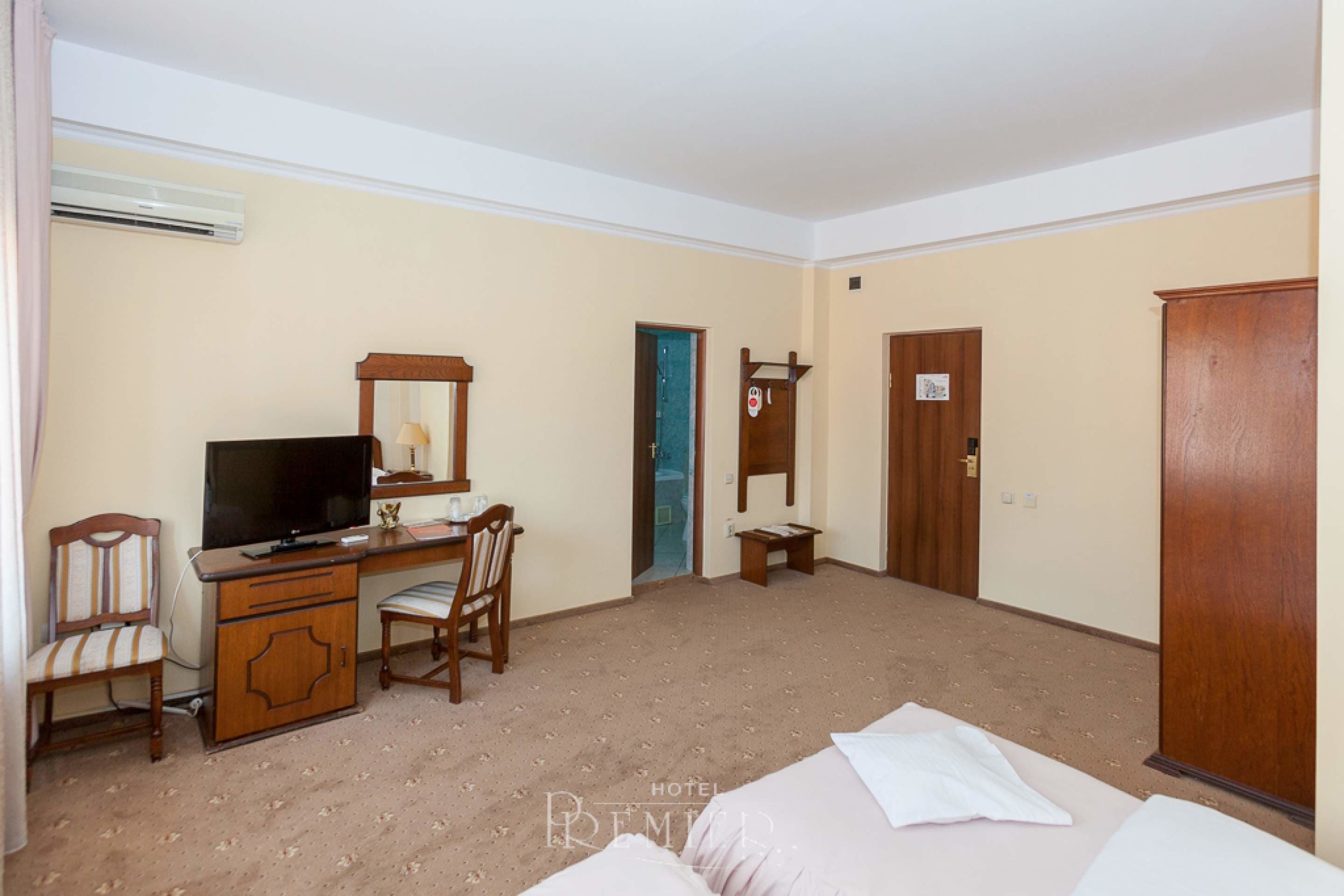 A hotel room with a bed, a desk, a chair, a television, and an air conditioning unit.
