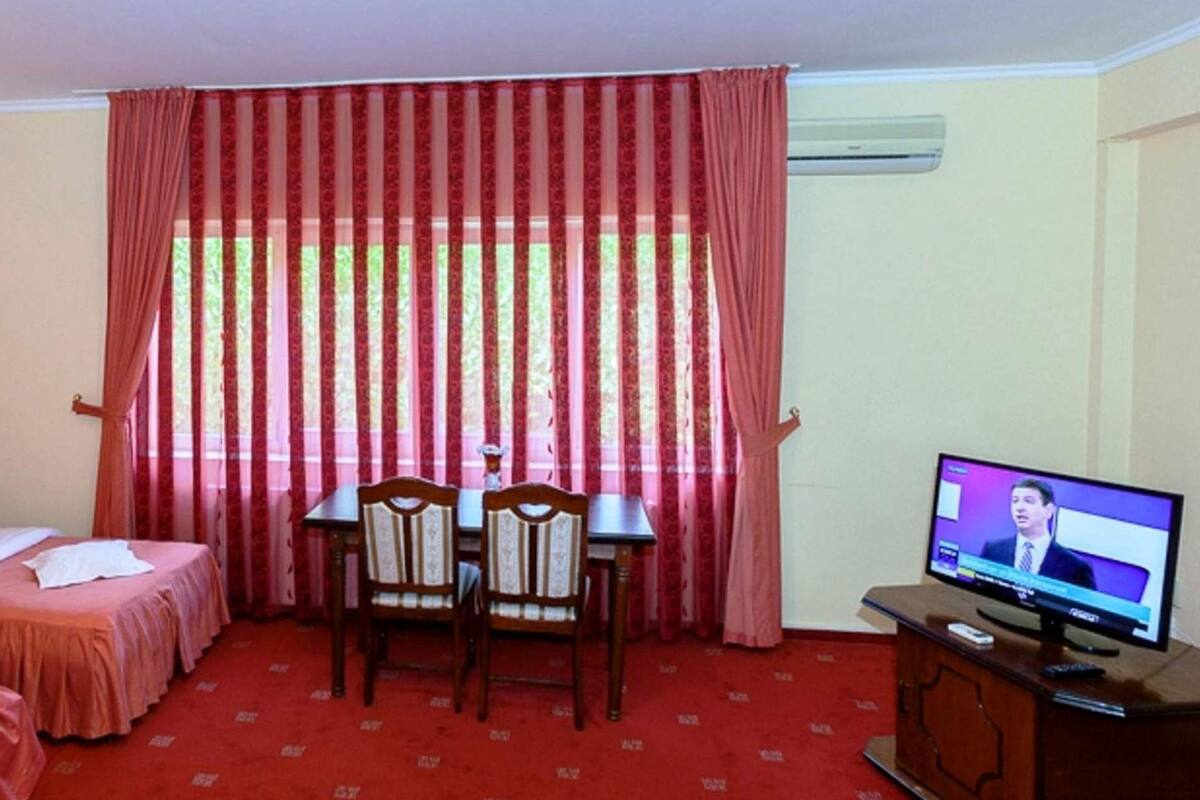 Ein Hotelzimmer mit zwei Betten, einem Schreibtisch, einem Sessel, einem Fernseher und einem Fenster mit Vorhängen.