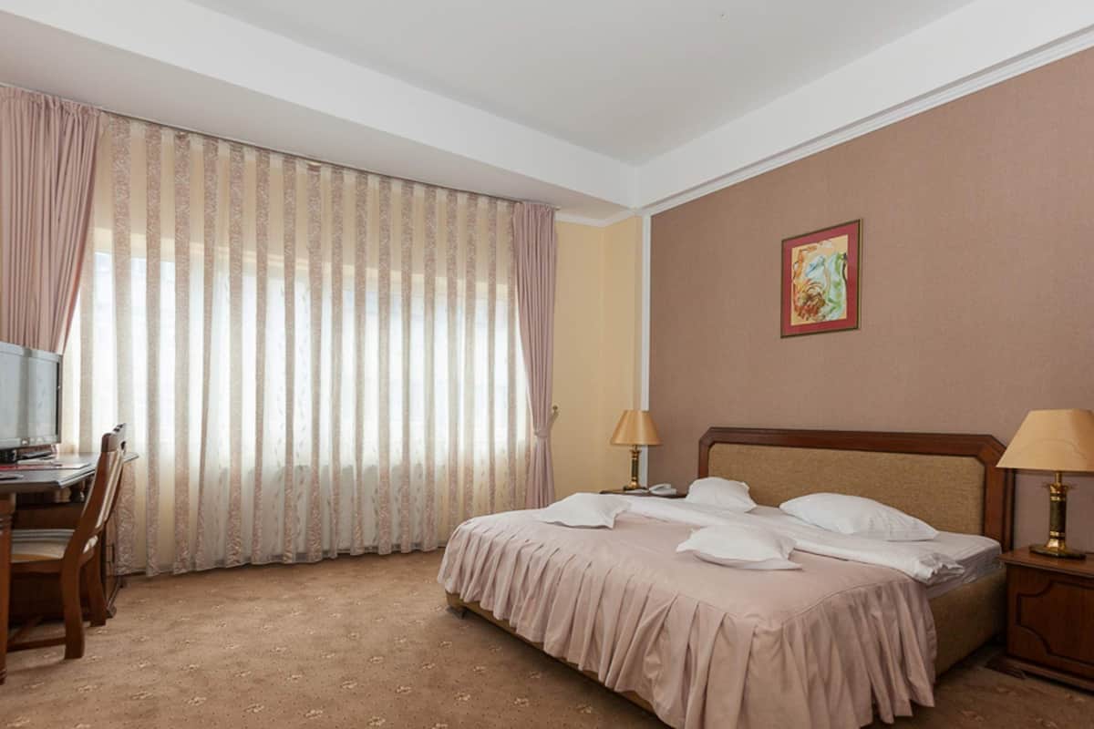 Ein Hotelzimmer mit einem Bett, einem Schreibtisch mit Computer, zwei Lampen und einem Bild an der Wand.