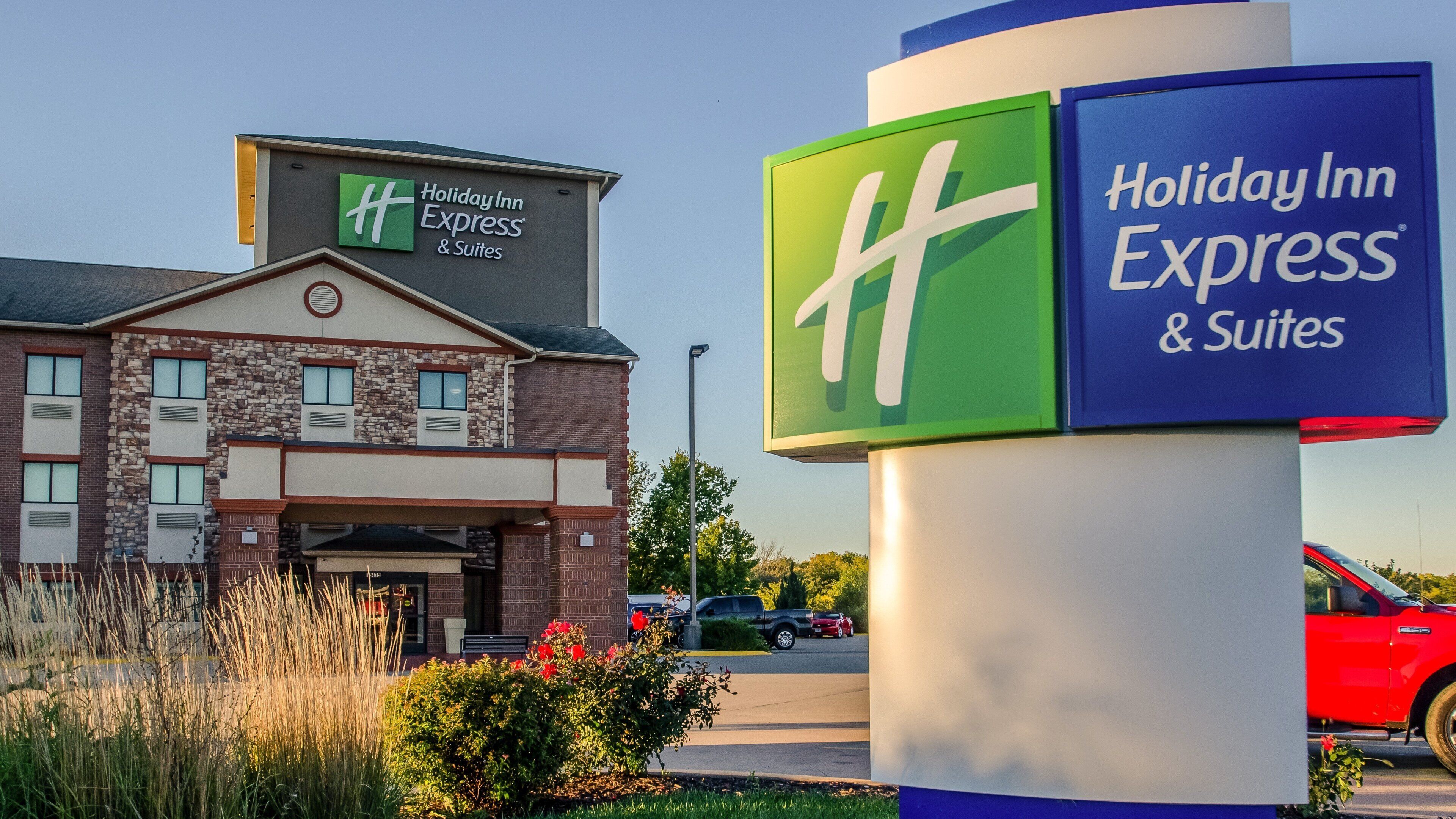 Holiday Inn Express & Suites -hotellin rakennus, jossa on selkeästi näkyvä kyltti, tiiliverhous ja pysäköintialue, jossa on autoja.