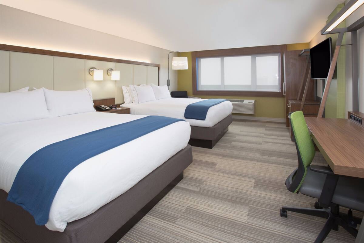 A hotel room with two beds, a desk, a chair, a TV, and a window.