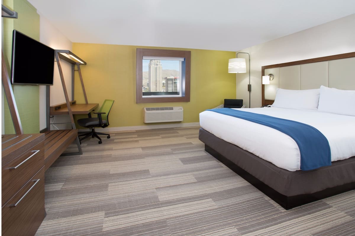 A hotel room with a bed, desk, chair, TV, and a window with a city view.