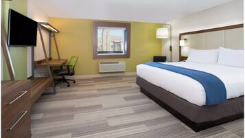 A hotel room with a bed, desk, chair, TV, and a window with a city view.
