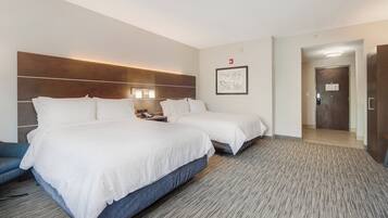 Habitación de hotel con dos camas, un escritorio con teléfono, una lámpara de pared y una puerta que da a otra habitación.