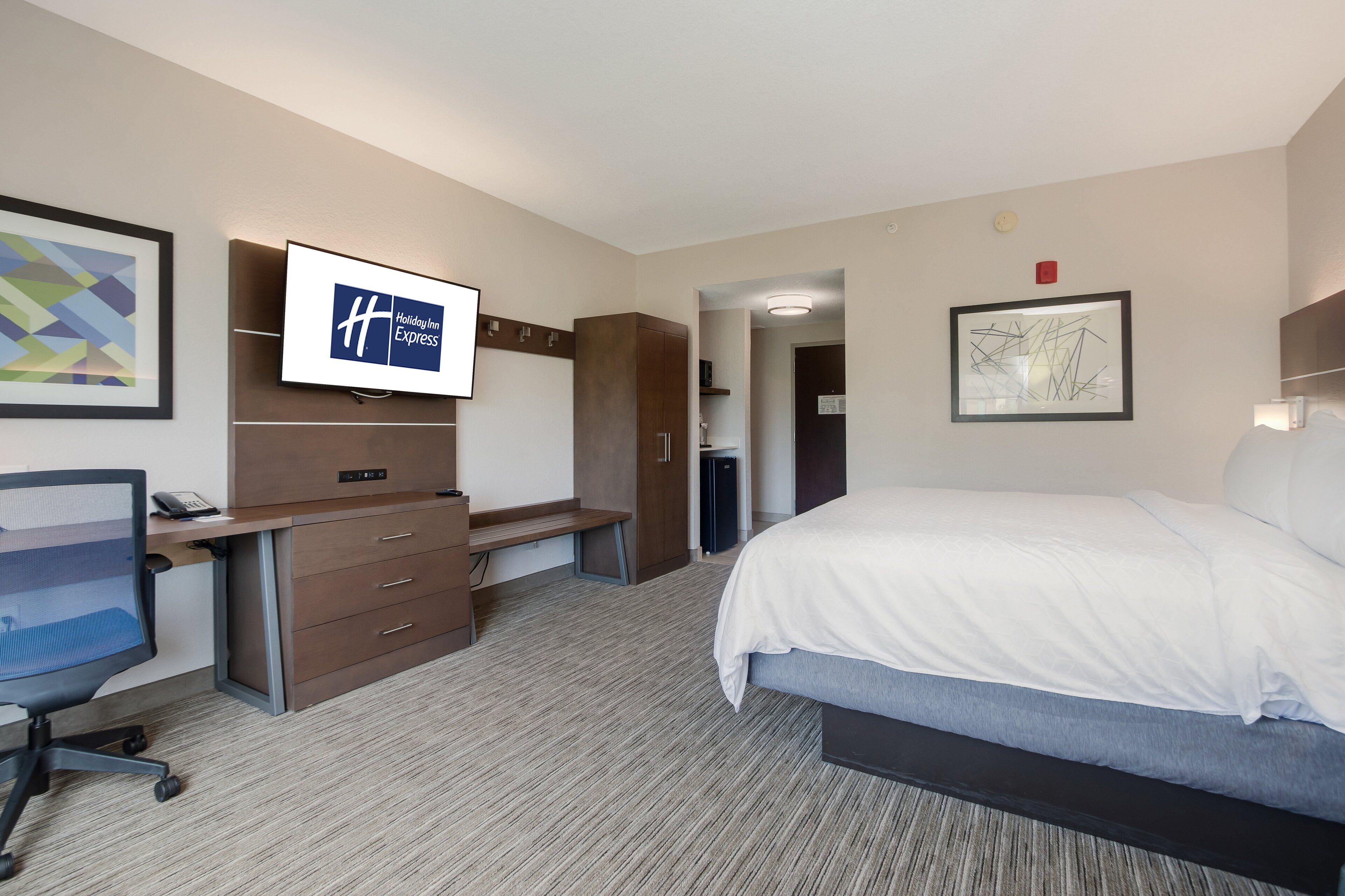 Ein Hotelzimmer mit Bett, Schreibtisch, Stuhl und Fernseher, der das Holiday Inn Express Logo zeigt.