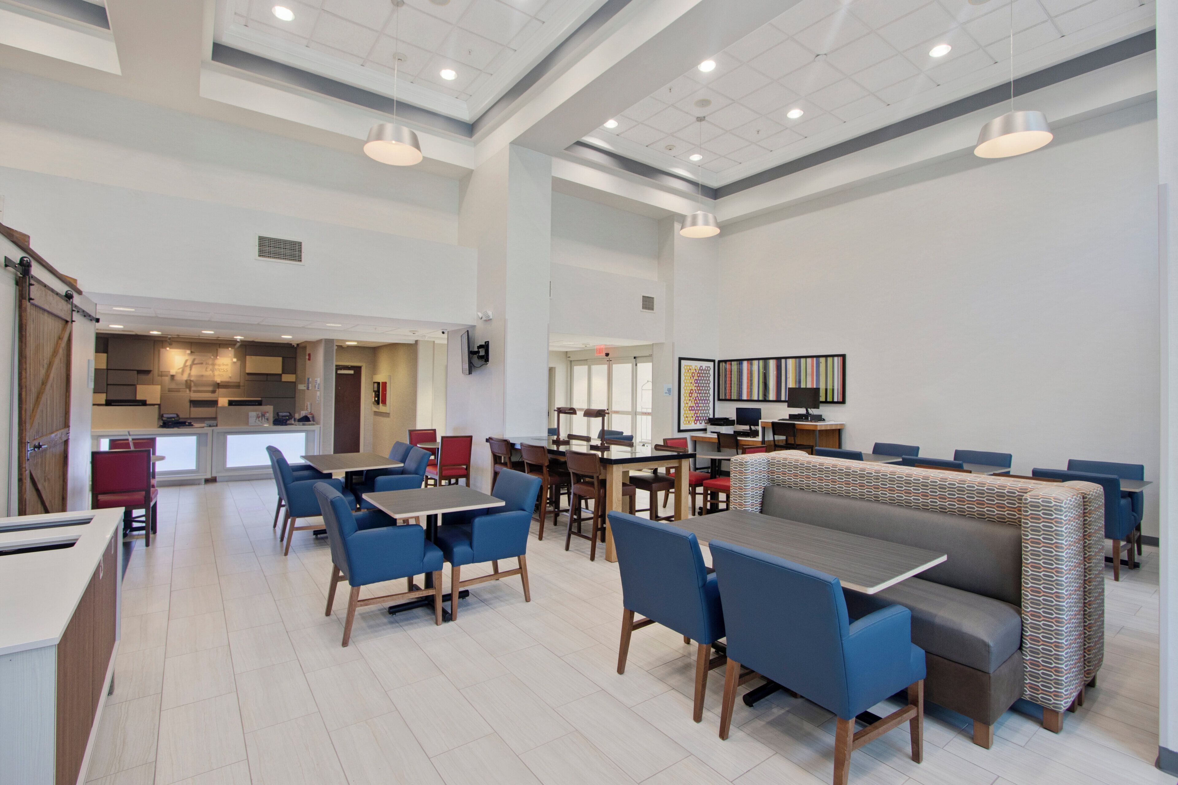 A spacious dining area with high ceilings, multiple tables and chairs, and a modern kitchen in the background.