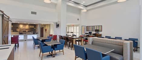 A spacious dining area with high ceilings, multiple tables and chairs, and a modern kitchen in the background.