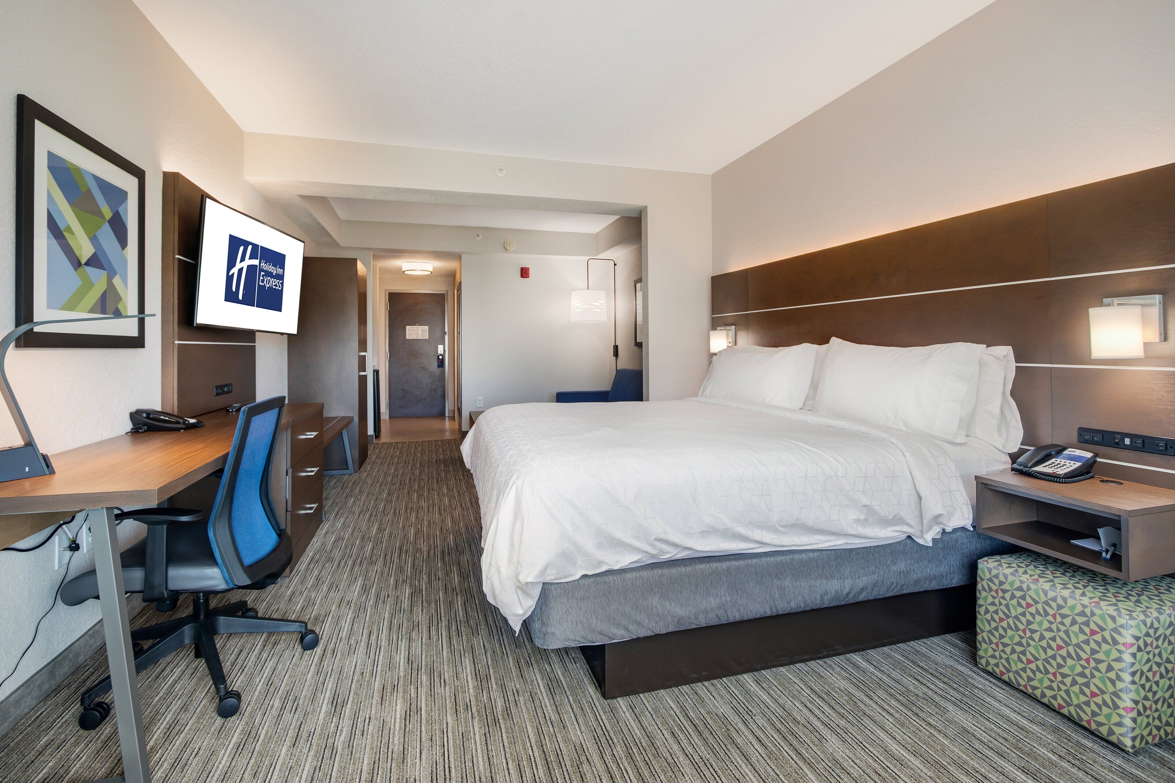 Une chambre d’hôtel équipée d’un lit, d’un bureau, d’une chaise et d’un téléviseur affichant le nom de l’hôtel.
