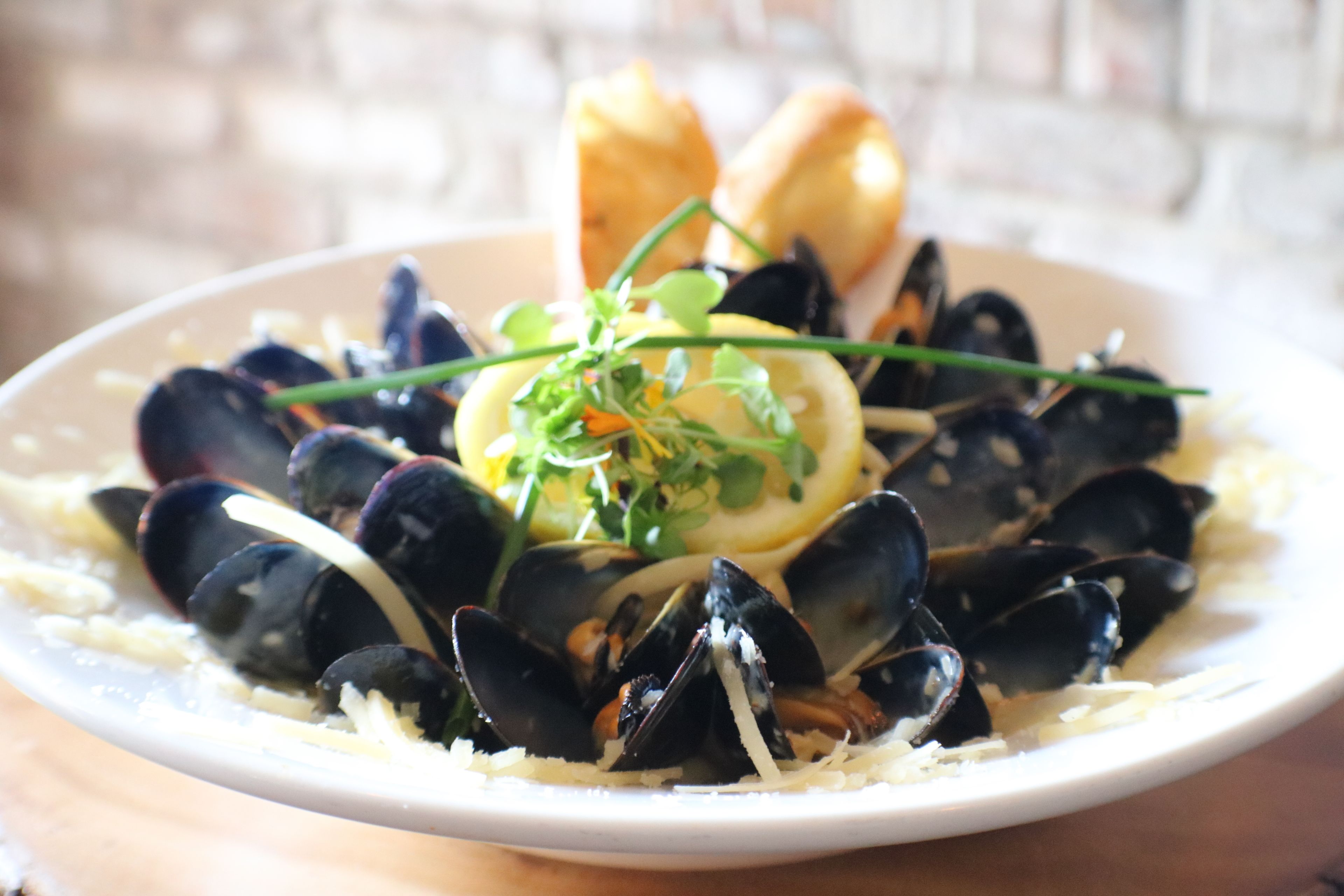 A plate of mussels with lemon slices and herbs, accompanied by bread.