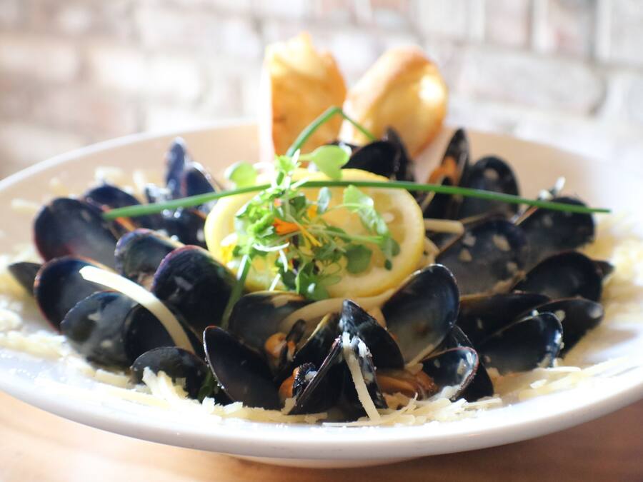 A plate of mussels with lemon slices and herbs, accompanied by bread.