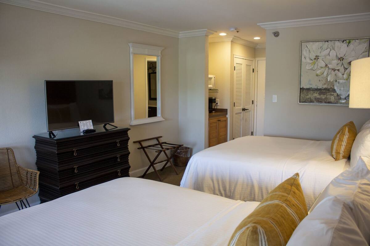 Quarto de hotel com duas camas, televisão, penteadeira e uma pequena mesa.