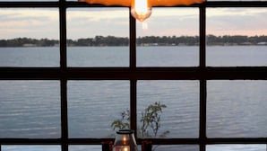 A table with a candle and a glass container, a window with a view of a body of water and trees, and a hanging lamp. - Inn On The Lakes (Sebring)