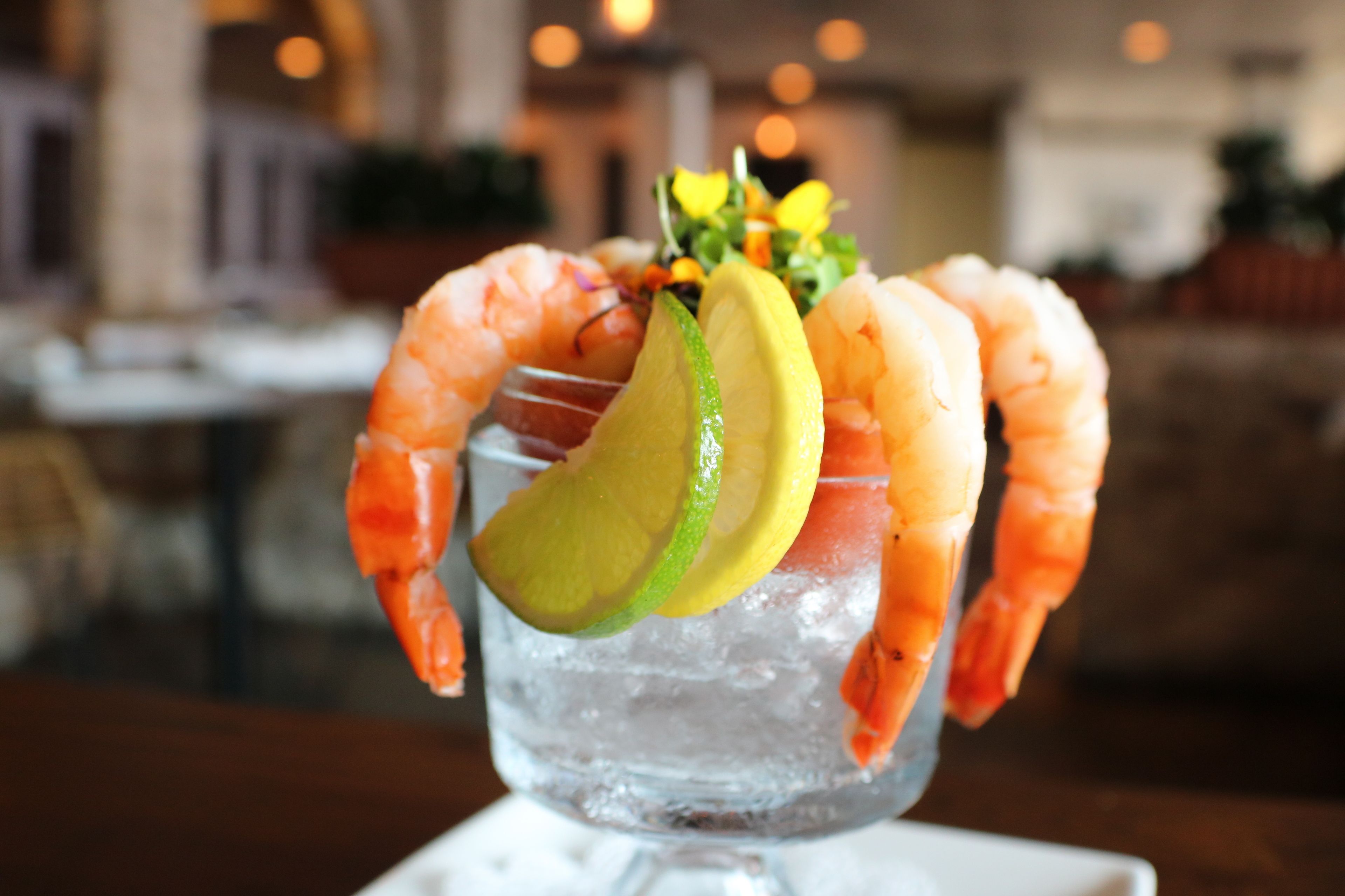 A cocktail with shrimp and lime garnish in a glass with ice.