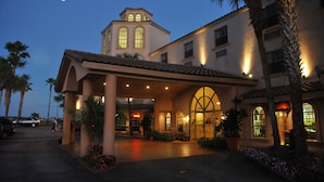 A hotel with a large arched entrance, a tower with windows, and palm trees. - Inn On The Lakes (Sebring)