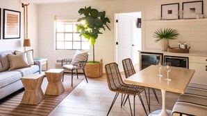 A modern living room with a sofa, coffee table, and chairs. There is a dining table with chairs and a potted plant. - Inn On The Lakes (Sebring)