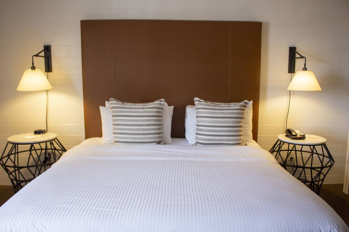 Quarto de hotel com uma cama grande, duas mesas de cabeceira com abajures e uma cabeceira.