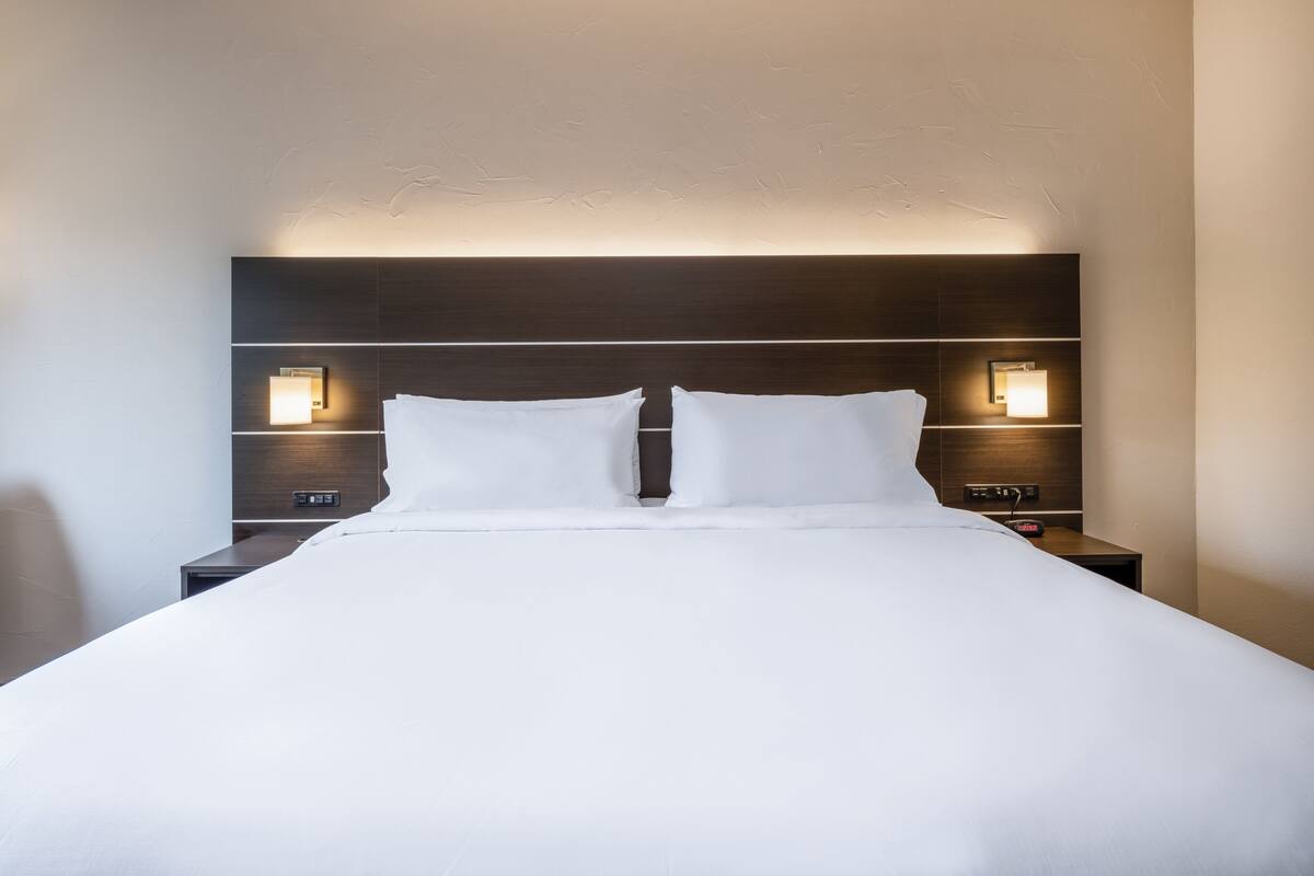 A neatly made bed in a hotel room with a dark headboard and two bedside lamps.