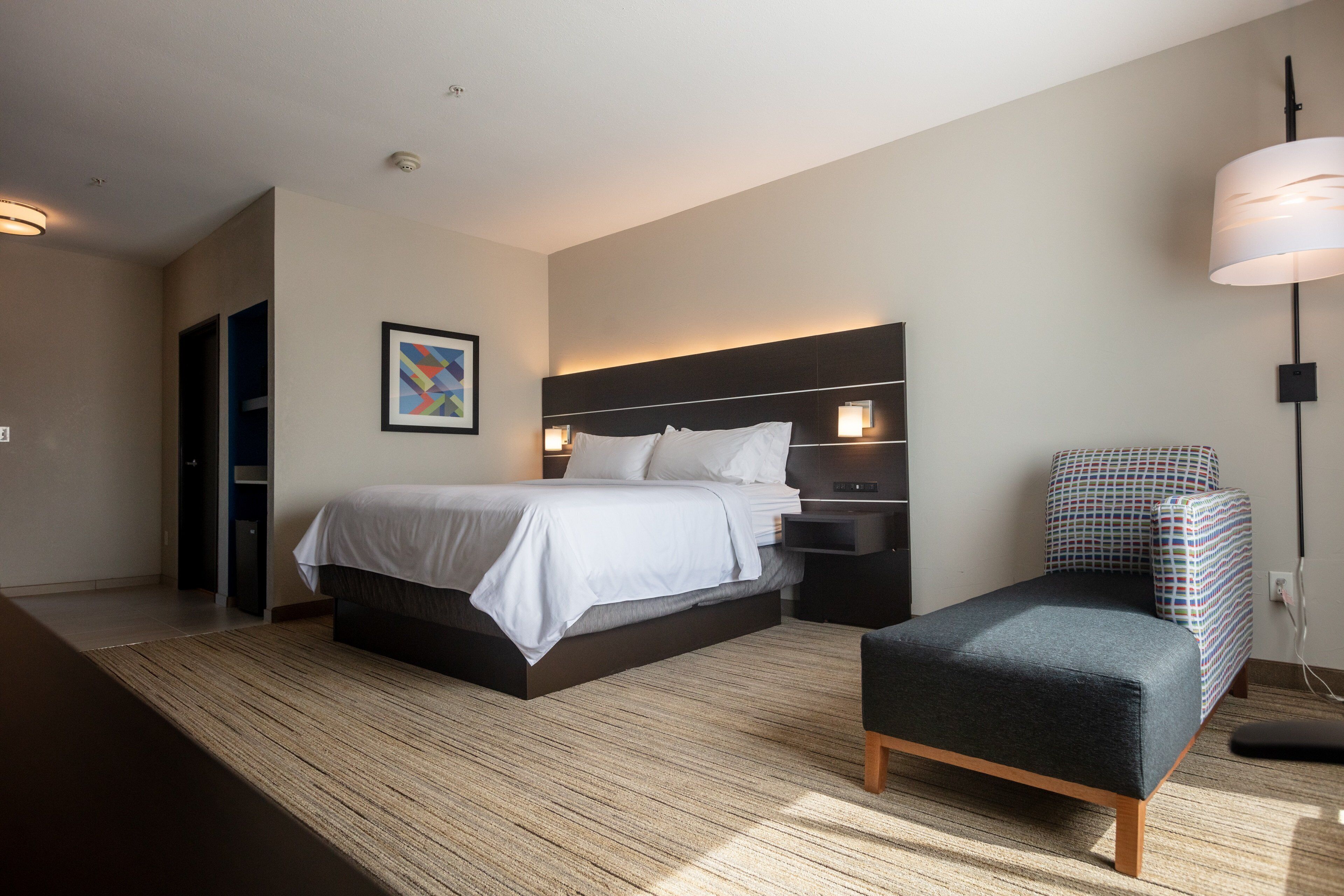 A modern hotel room with a large bed, bedside tables, a desk, and a chair.