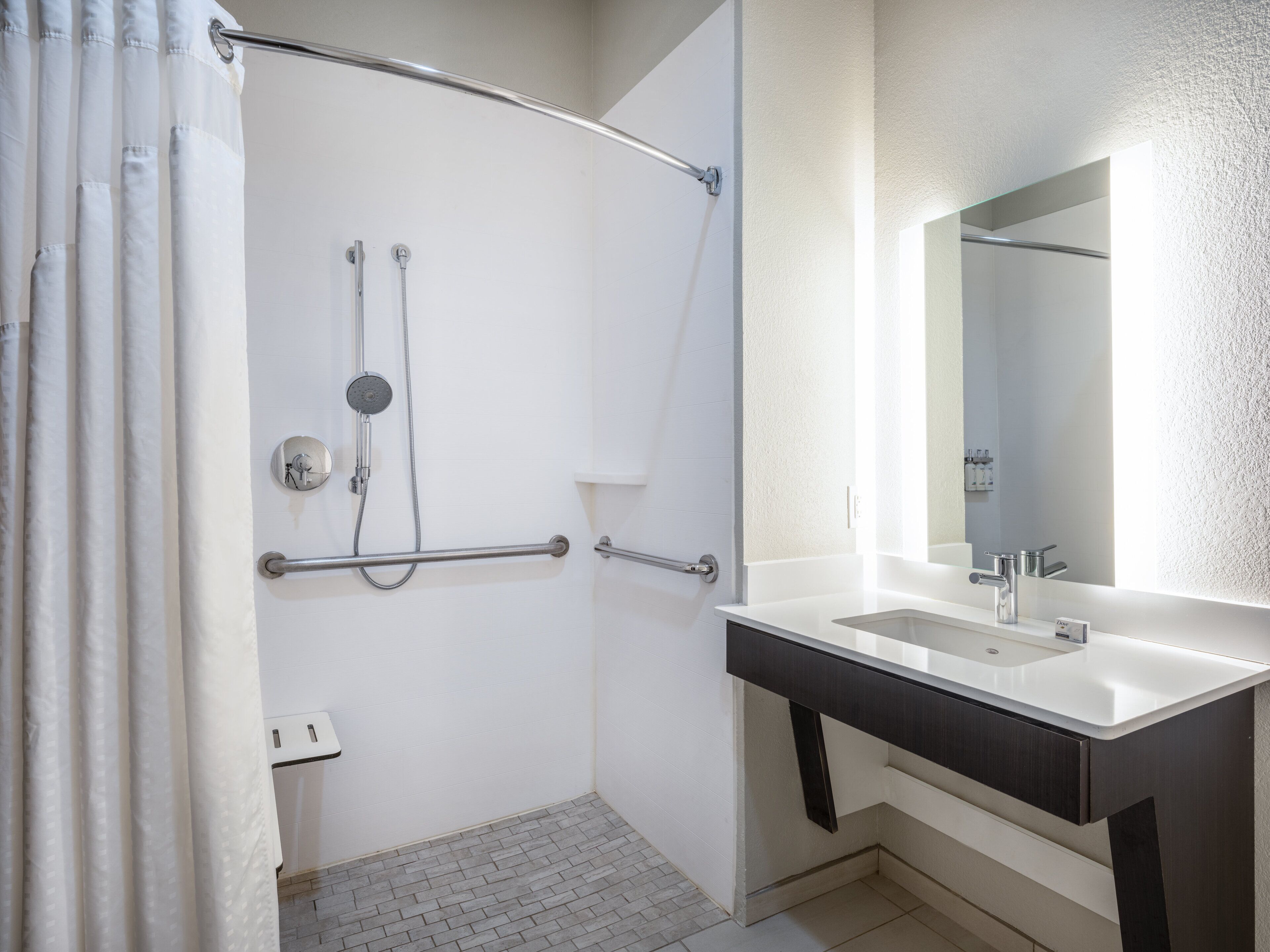 A modern bathroom with a shower, grab bars, a sink, and a mirror.