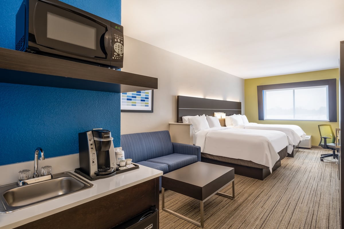 A hotel room with a kitchenette, a bed, a sofa, a coffee maker, and a window.