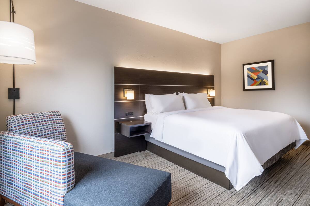 A hotel room with a large bed, a bedside table, a chair, and a lamp.