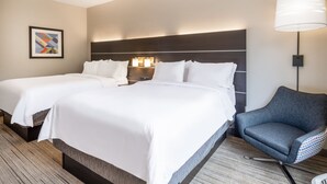 Habitación de hotel con dos camas, una silla y una lámpara fijada a la pared.