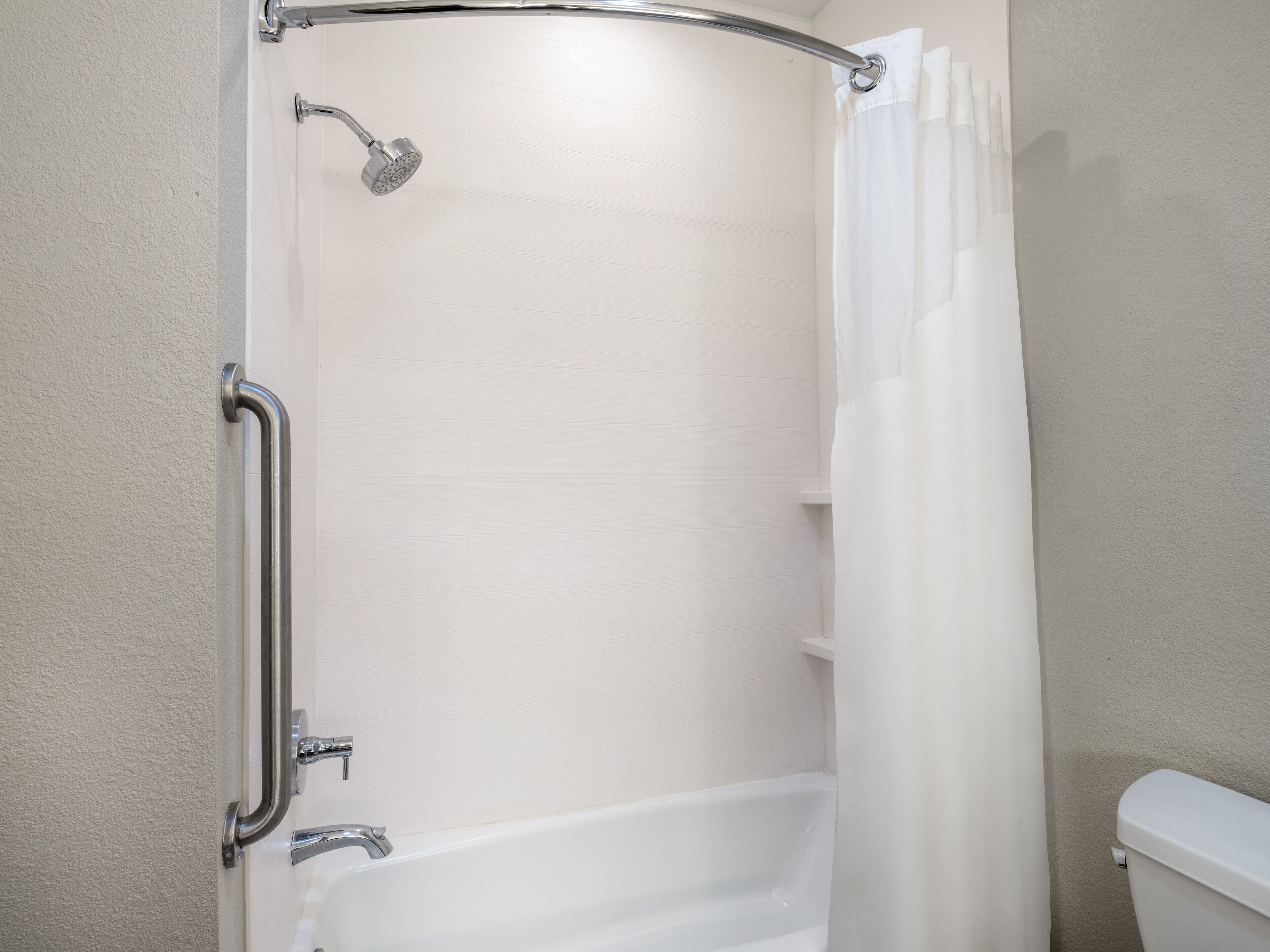 A bathroom with a shower, toilet, and grab bar.