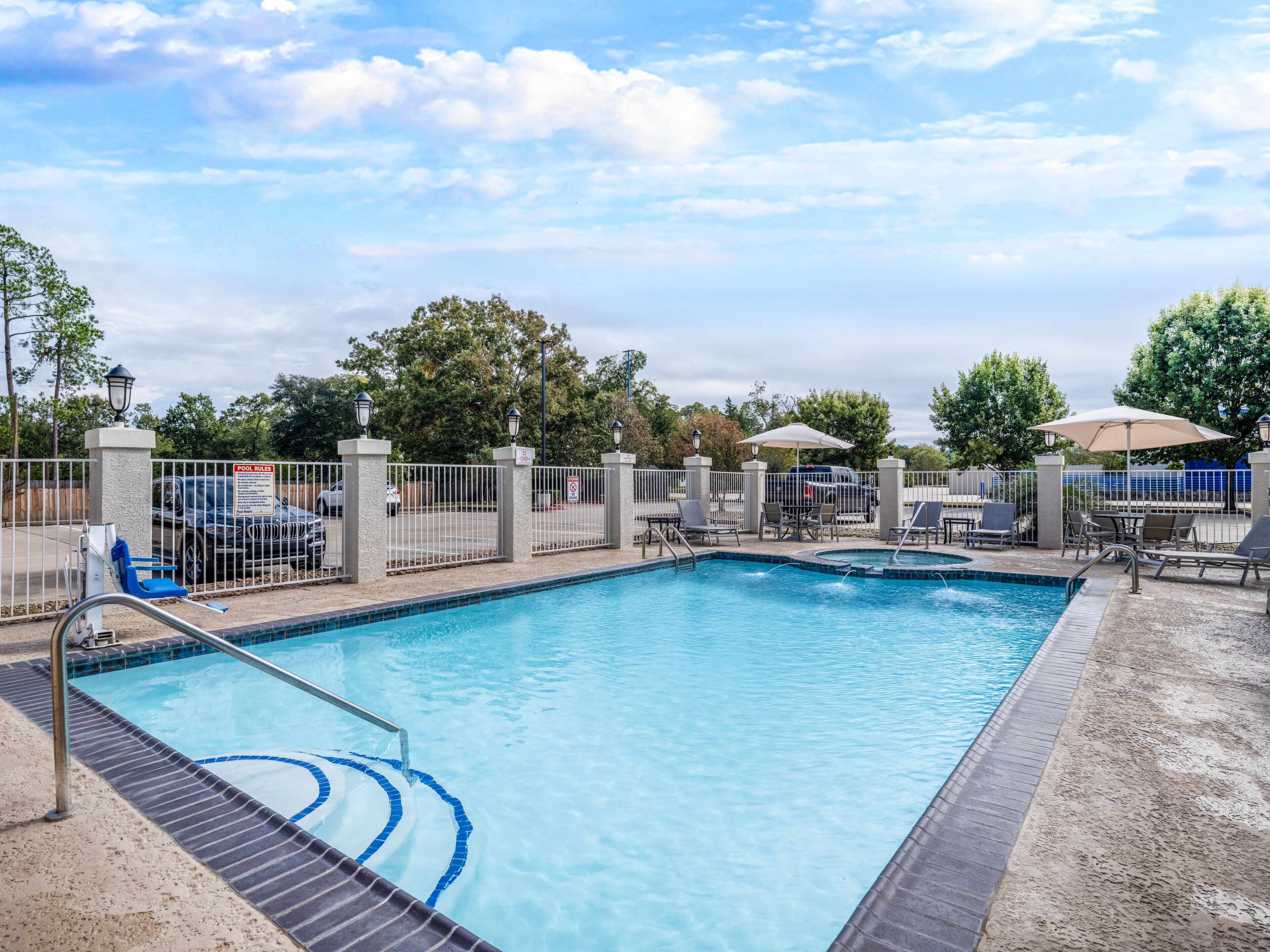 A swimming pool with a tiled deck, a fenced area, and lounge chairs.