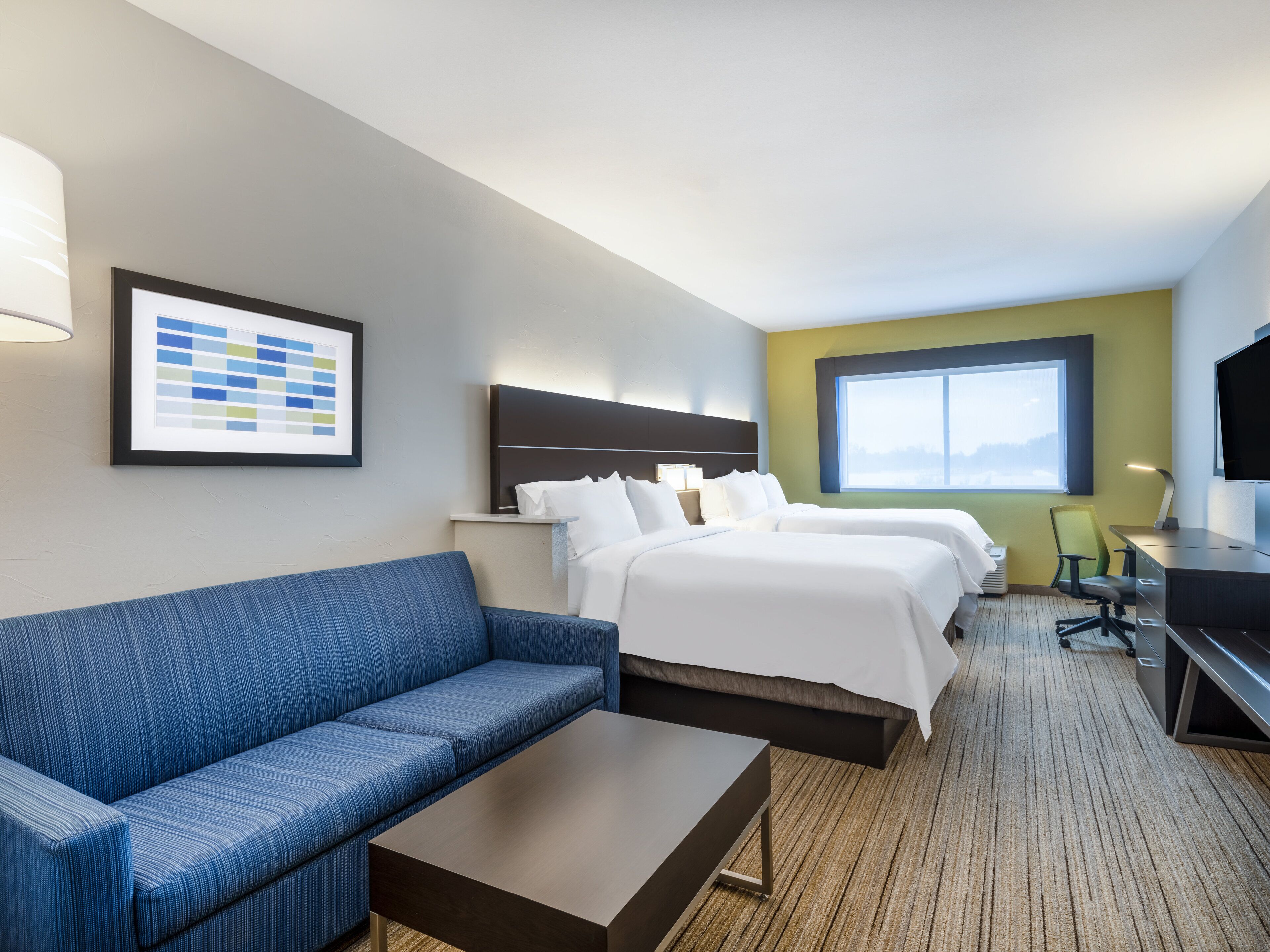 Ett hotellrum med en blå soffa, två sängar, ett skrivbord och ett stort fönster.