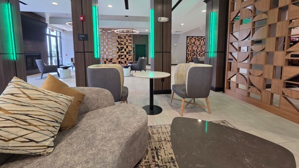 Un hall d’hôtel moderne, doté d’un canapé, de fauteuils, d’une table ronde et d’un mur décoratif orné de motifs géométriques.