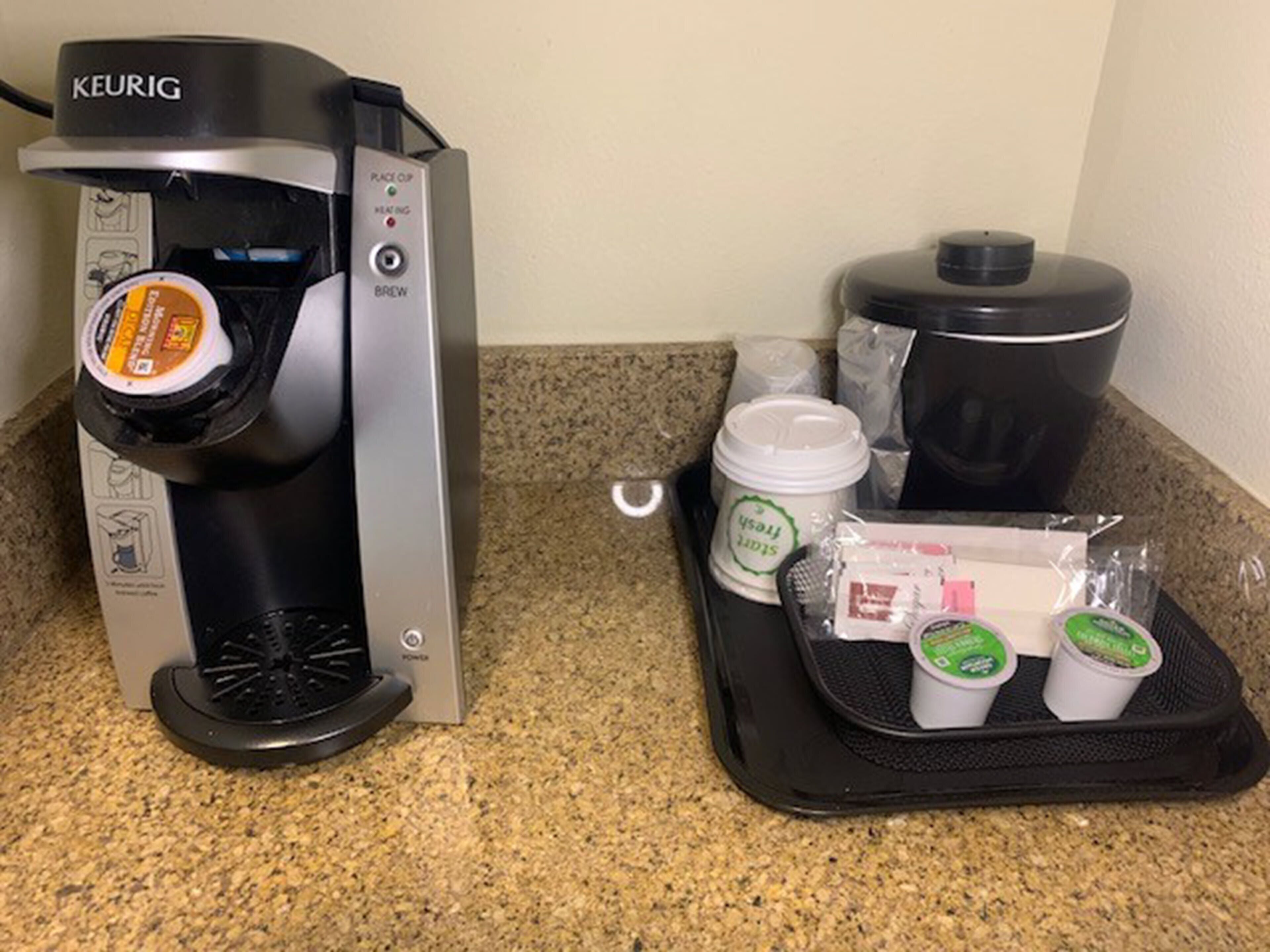 A Keurig coffee maker with a pod, a coffee pot, and a tray with coffee cups and a container.