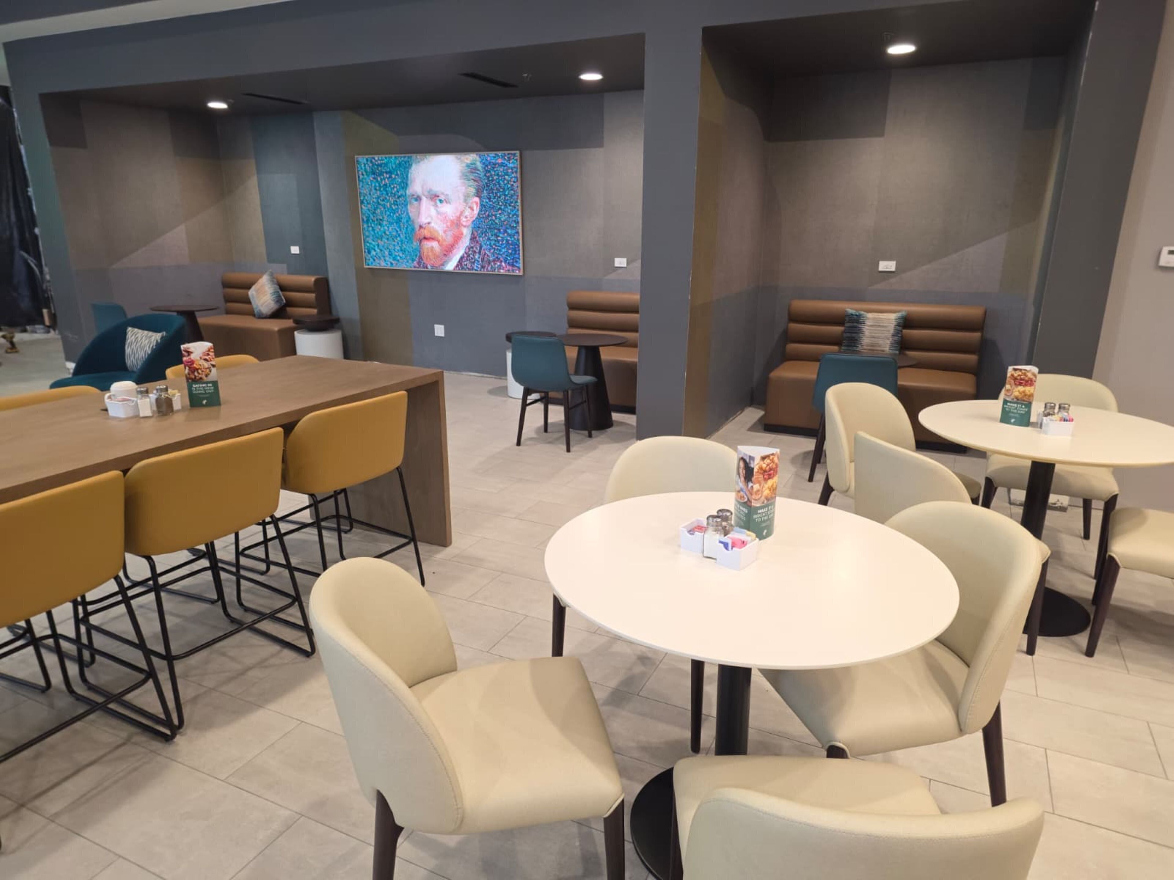 A modern lounge area with seating arrangements including a long table and several round tables, each with a menu stand.