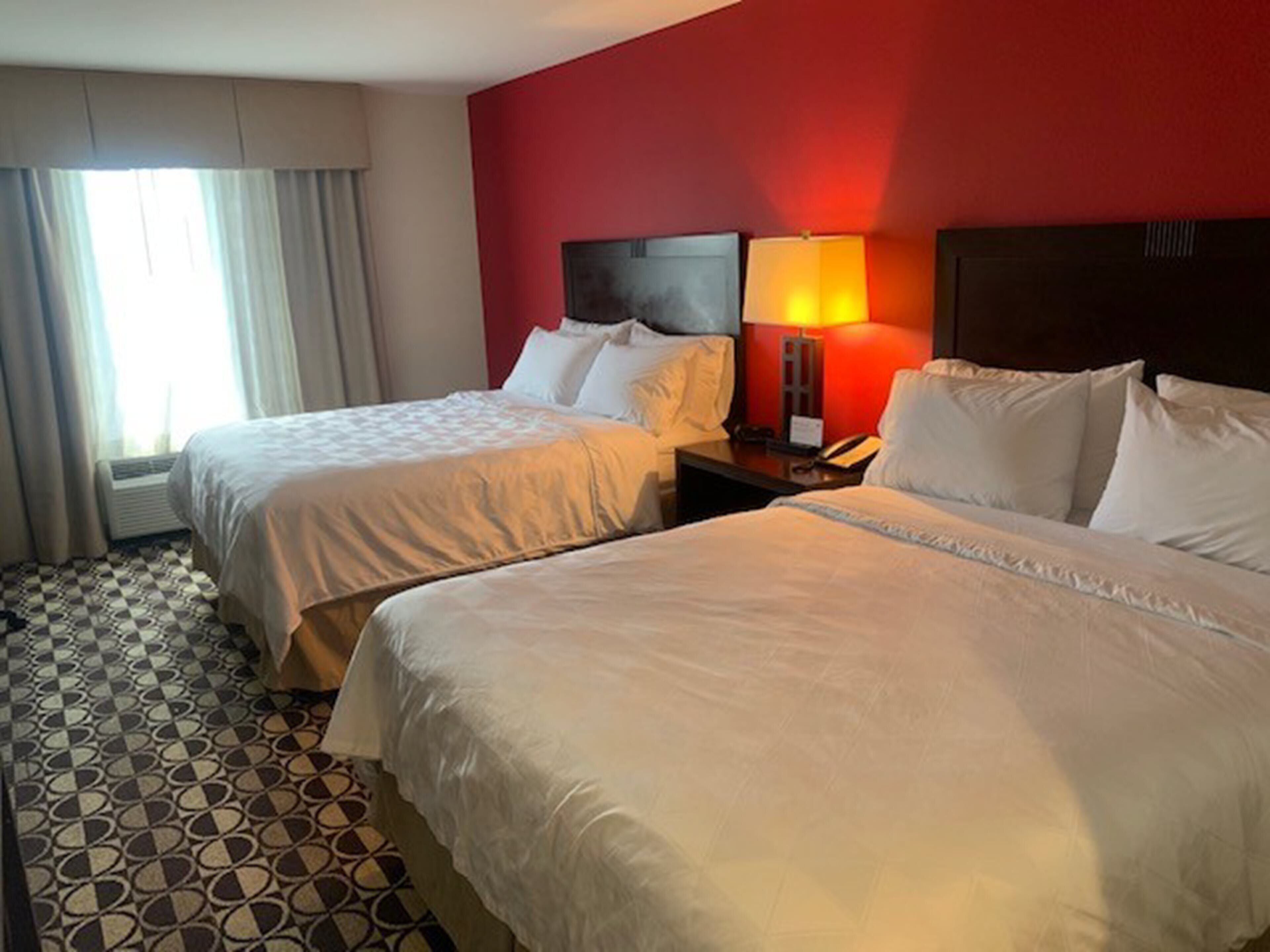 Una habitación de hotel con dos camas, una mesita de noche con lámpara y una ventana con cortinas.