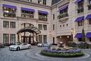 Entrada de un hotel con una fuente, un automóvil y una persona de pie cerca de la entrada.