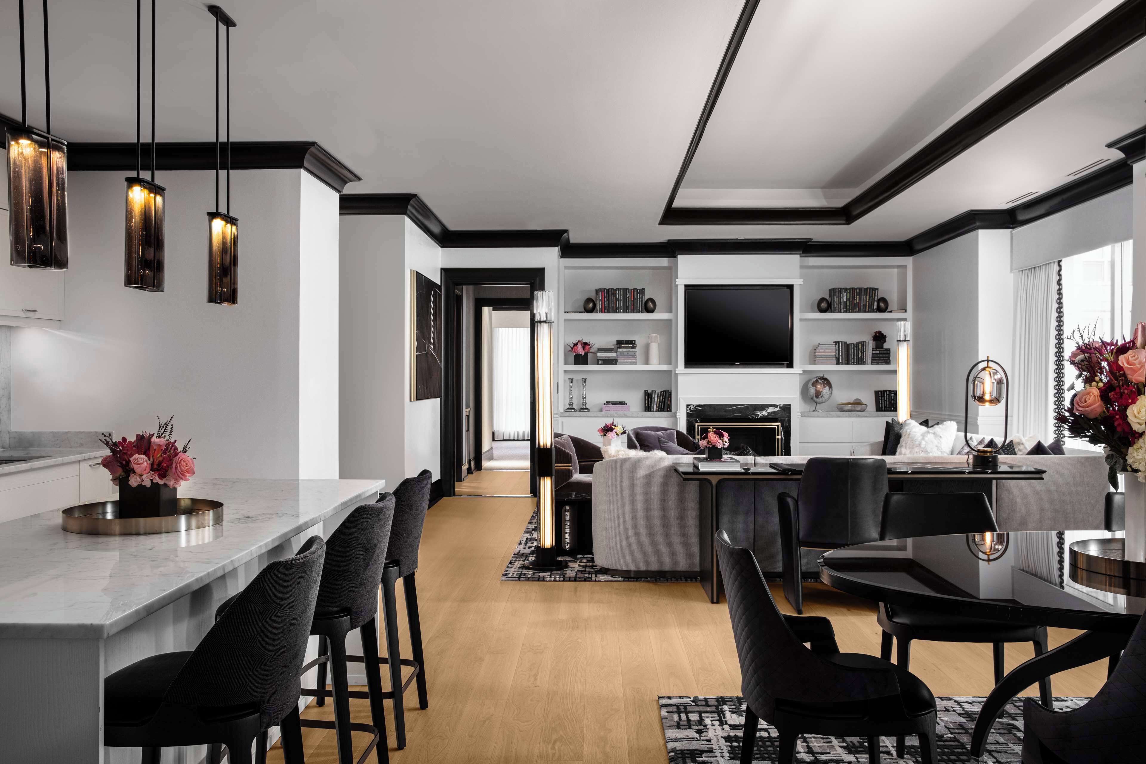 A modern kitchen with a marble countertop, black bar stools, and pendant lighting.