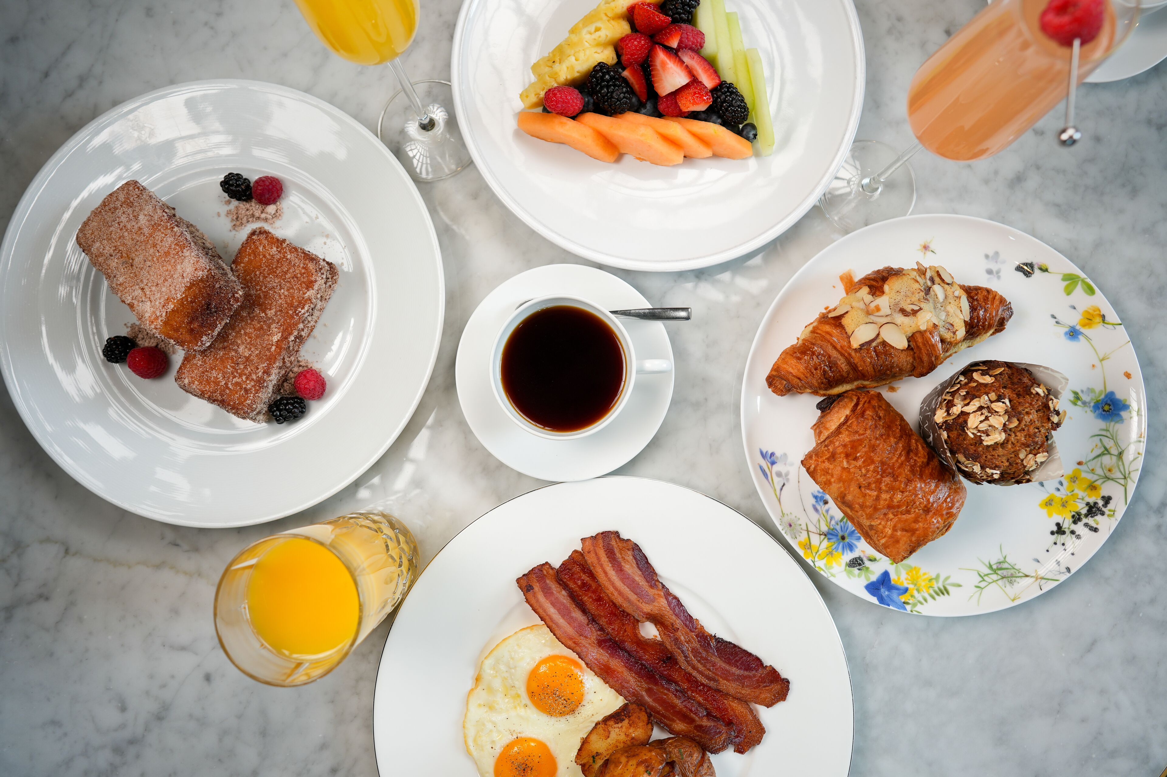 Una mesa de desayuno con diversos platos, incluyendo tostadas, huevos, tocino, pastelería y fruta.