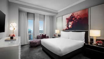 A modern hotel room with a large bed, a desk, a chair, and a view of the city.