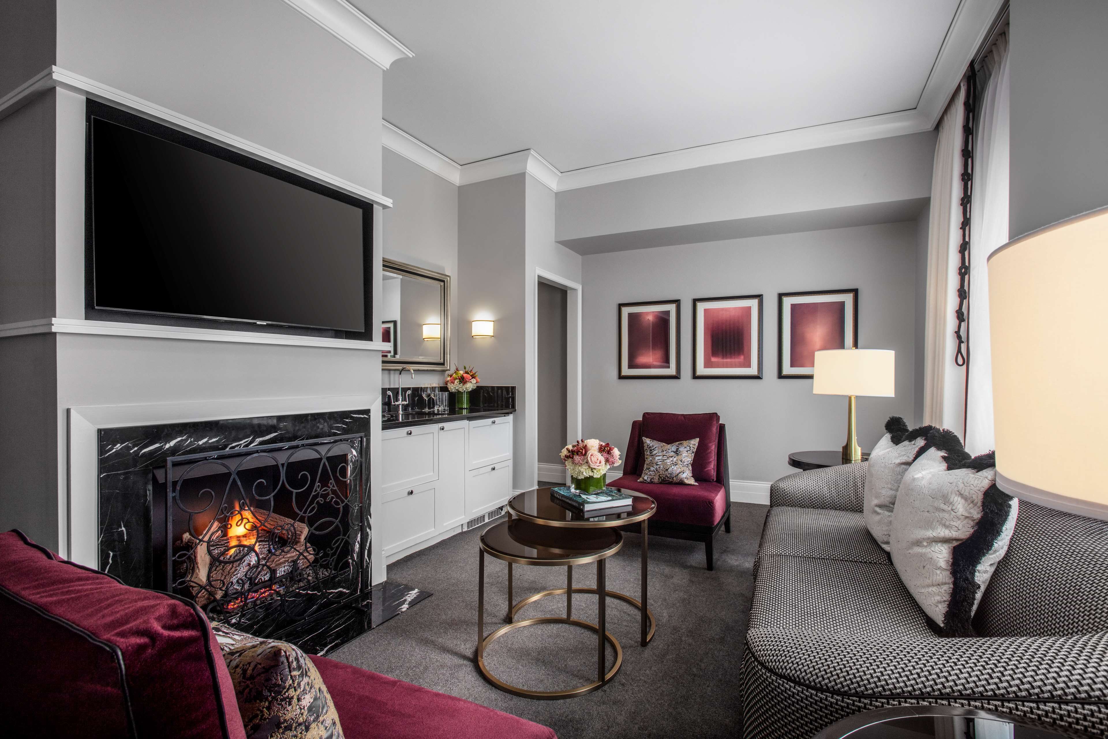 A living room with a fireplace, a sofa, a red armchair, a coffee table, and framed artwork on the wall.