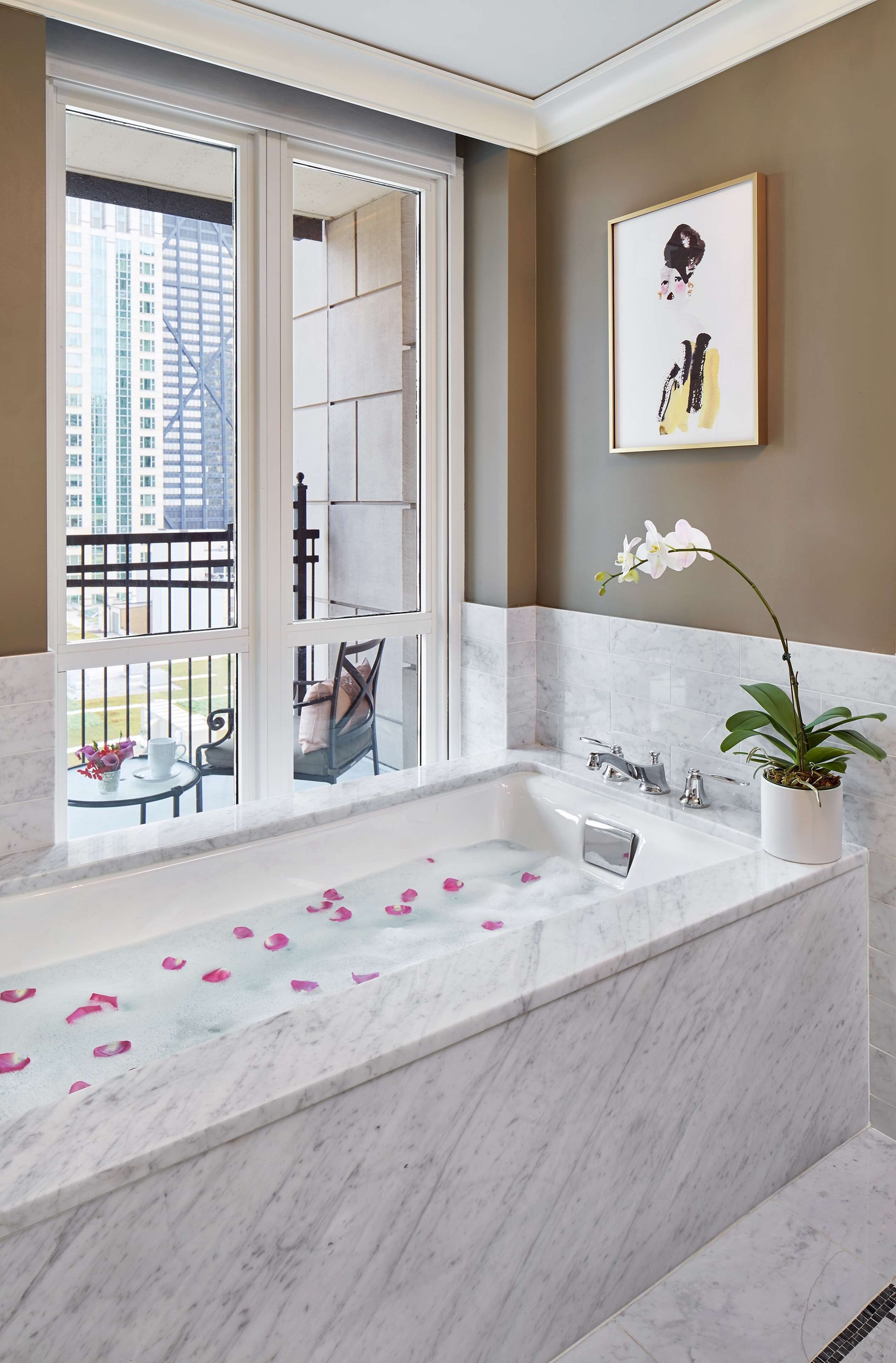 Une salle de bain avec une grande baignoire, une orchidée en pot et une œuvre d’art encadrée accrochée au mur.