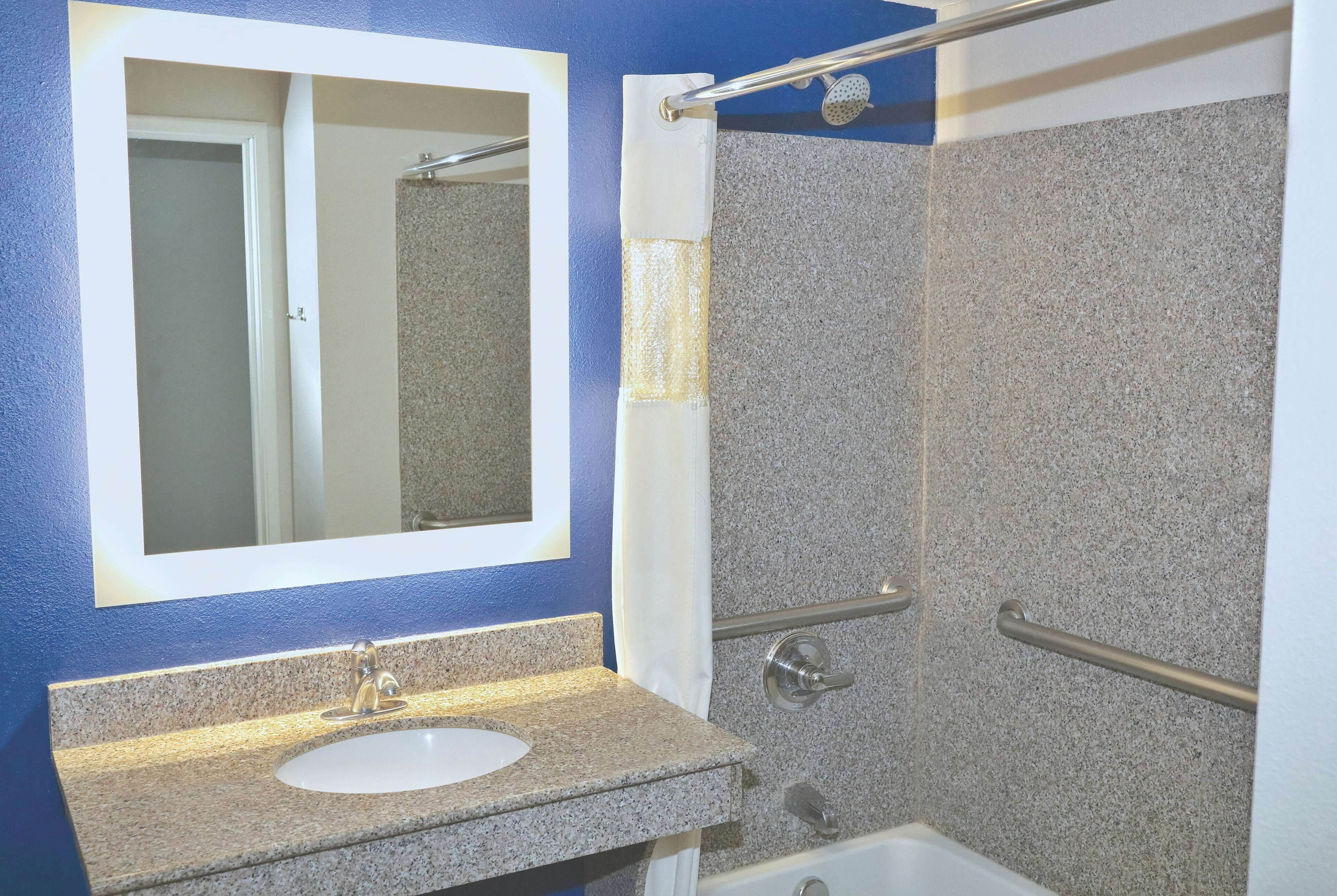 Un baño con lavamanos, espejo, ducha y barras de apoyo.