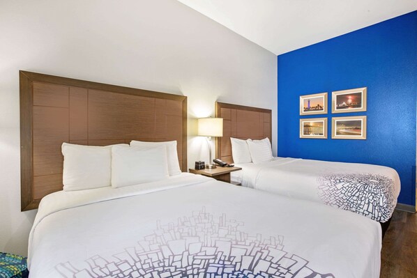 A hotel room with two beds, a wooden headboard, a nightstand with a lamp, and four framed pictures on the wall.