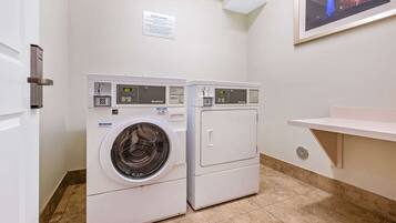 A laundry room with two front-loading washing machines, a sign indicating guest laundry, and a framed picture on the wall.