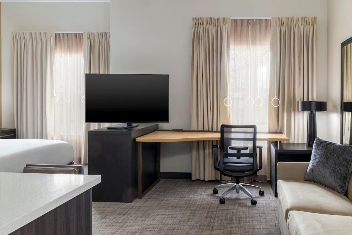 A hotel room with a bed, a desk with a computer, a TV, a chair, and a sofa.