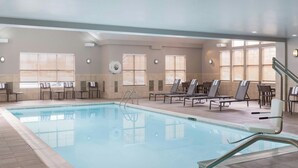 An indoor swimming pool with clear water, surrounded by lounge chairs and tables, and large windows providing natural light.