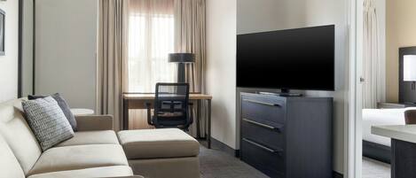 A hotel room with a sofa, a desk with a chair, a flat-screen TV, a dresser, and a bed.