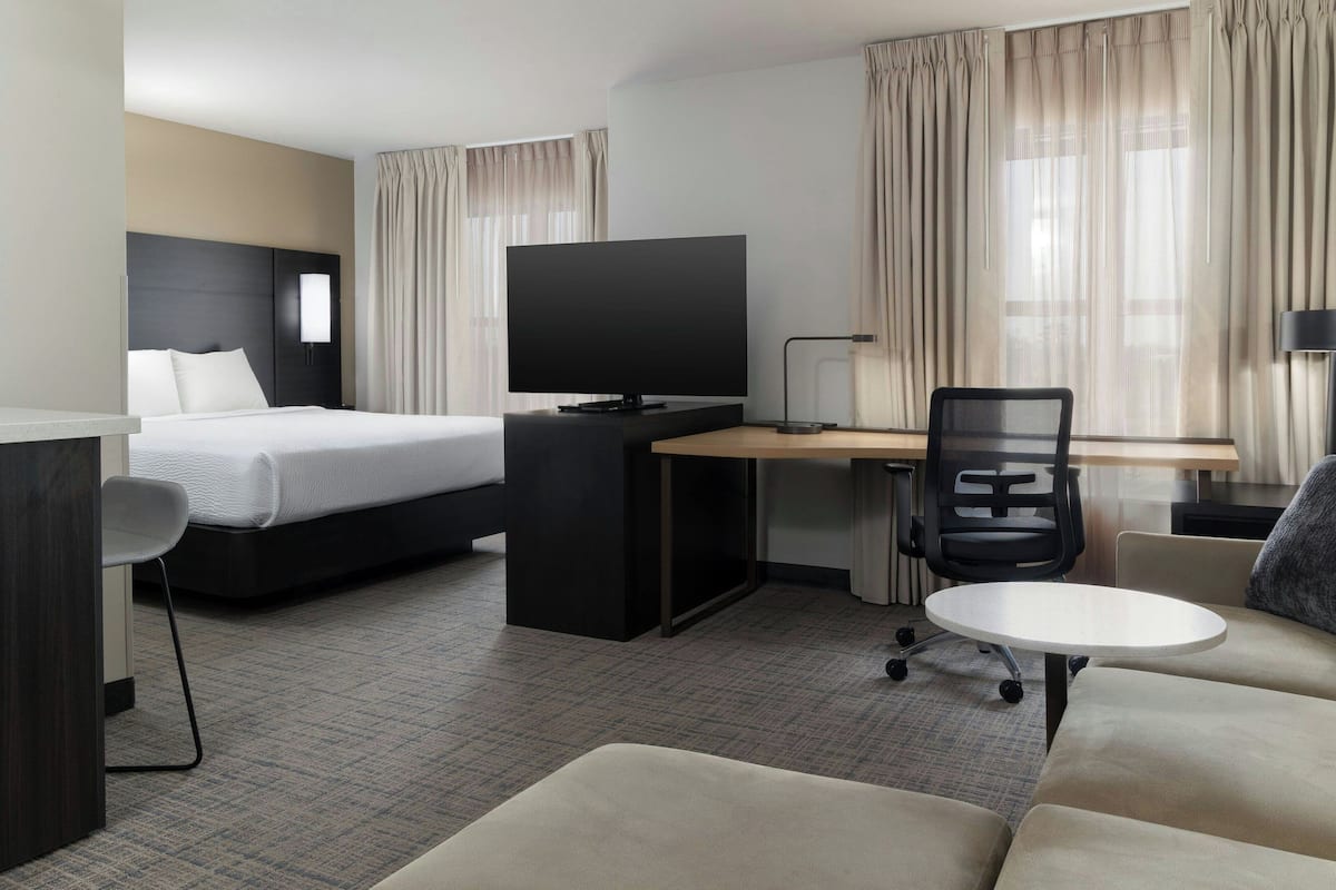 A hotel room with a bed, a desk with a computer, a TV, a chair, and a small table.