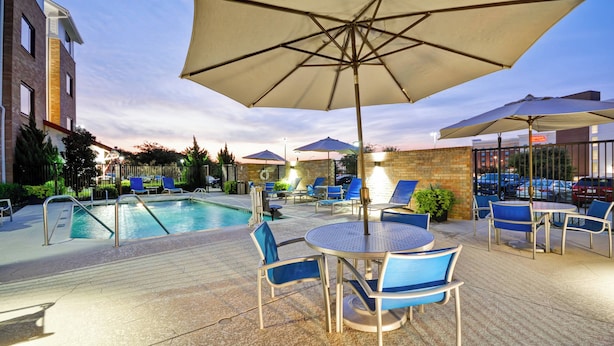 Un espace aménagé au bord de la piscine, avec des chaises longues et des parasols, une piscine et un mur en briques.